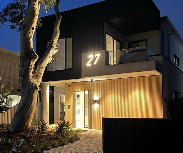 Modern two-storey home façade at night with an illuminated house number and warm entry lighting